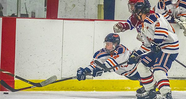 Junior forward Tyler Paige (12) leaps and extends his stick to knock away a loose puck in the neutral zone against Natick.