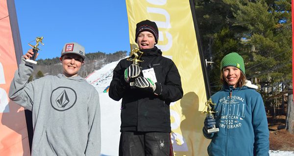 Ethan Sveen (center) hoists his trophy in celebration after placing first in the U14 boys giant slalom. Photos by Cranmore Mountain