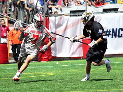 Luke Buckley (7) navigates through a stick check behind the cage during Ohio State’s 9-6 loss to Maryland in Monday’s title game. – Luke Buckley (7) goes one-on-one with a Towson long-pole and makes a cut to the cage during Ohio State’s 11-10 win over the Tigers in Saturday’s Division I National Semifinals at Gillette Stadium. Photos by Michael Flanagan