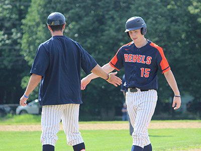 Brian Gaughan (15) is congratulated by his first base coach after an RBI single during the bottom of the fifth. Photos by Michael Flanagan
