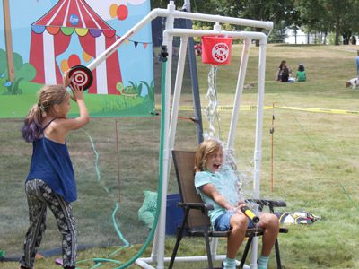 After a girl pushes the target, a bucket of water pours over her friend’s head at the Dover Days fair.