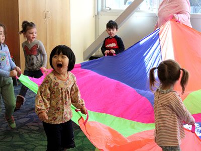 A group of preschoolers at the Walpole Public Library play with a giant neon parachute after a Thanksgiving-themed storytime. Photos by Laura Drinan