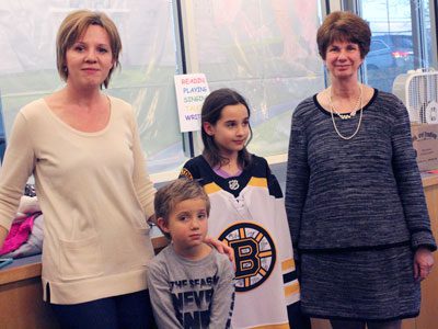 Emma celebrates her win of an autographed Bruins jersey and certificate of authenticity from the Bruins’ ‘When You Read, You Score!’ program with her mother, brother, and librarian, Paula Dugan.