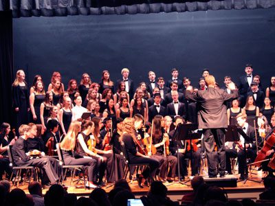 Jonathan VanderWoude conducts a full stage of orchestra and chorus students Needham High’s winter concert.