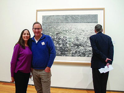 Suzanne and Lloyd Kahan of Wayland view the Christiane Baumgarten exhibit 'Another Country,' after the conclusion of the Boston Symphony Orchestra’s Community Concert at the Davis Museum, Wellesley College. Behind the Kahans is 'Another Country,' a woodcut by Christiane Baumgartner with Juliette Kaiser. Photos by Audrey Anderson