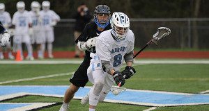 Connor DePiero (8) scoops a groundball off of a face-off with Dover-Sherborn’s Matt Paolatto hot in pursuit. Photo by Denise DePiero.