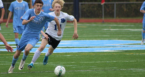 Medfield’s James Layden (20) moves the ball through the middle with Dover-Sherborn’s Wyatt Goldfisher (14) hot on his tail.